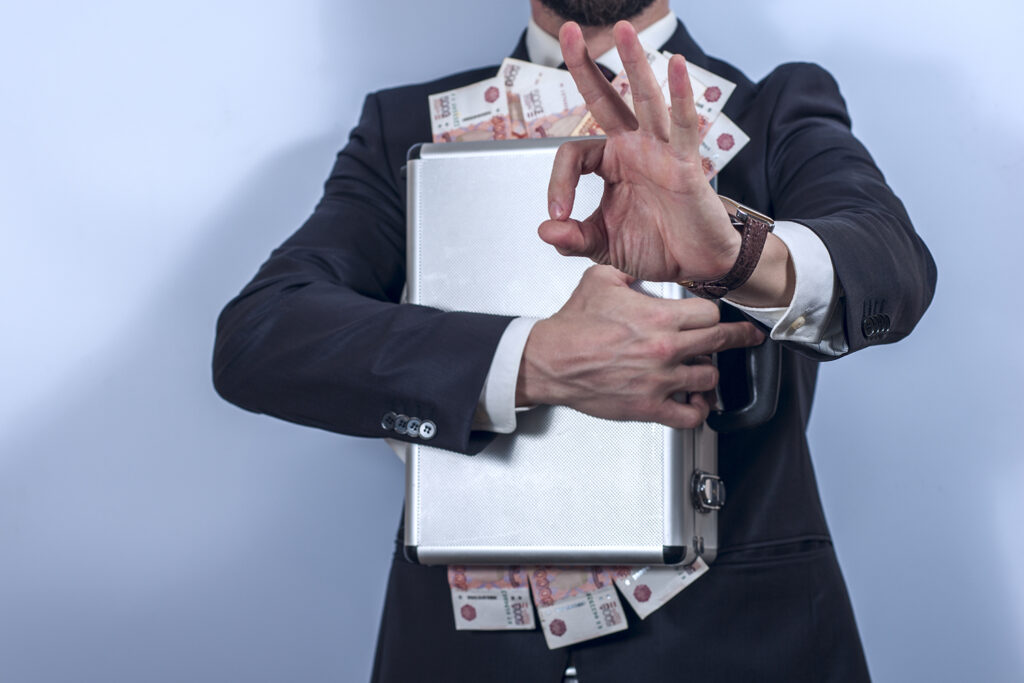 Man in suit holds metal briefcase full of money